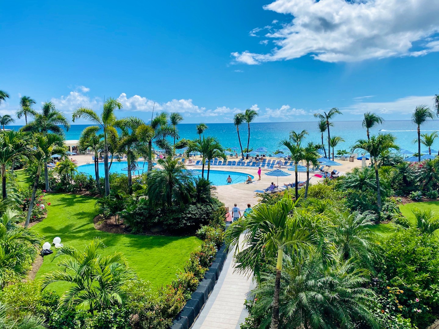 Lush green towards pool with palm trees and sea view of Maho Beach at Royal Islander La Terrasse